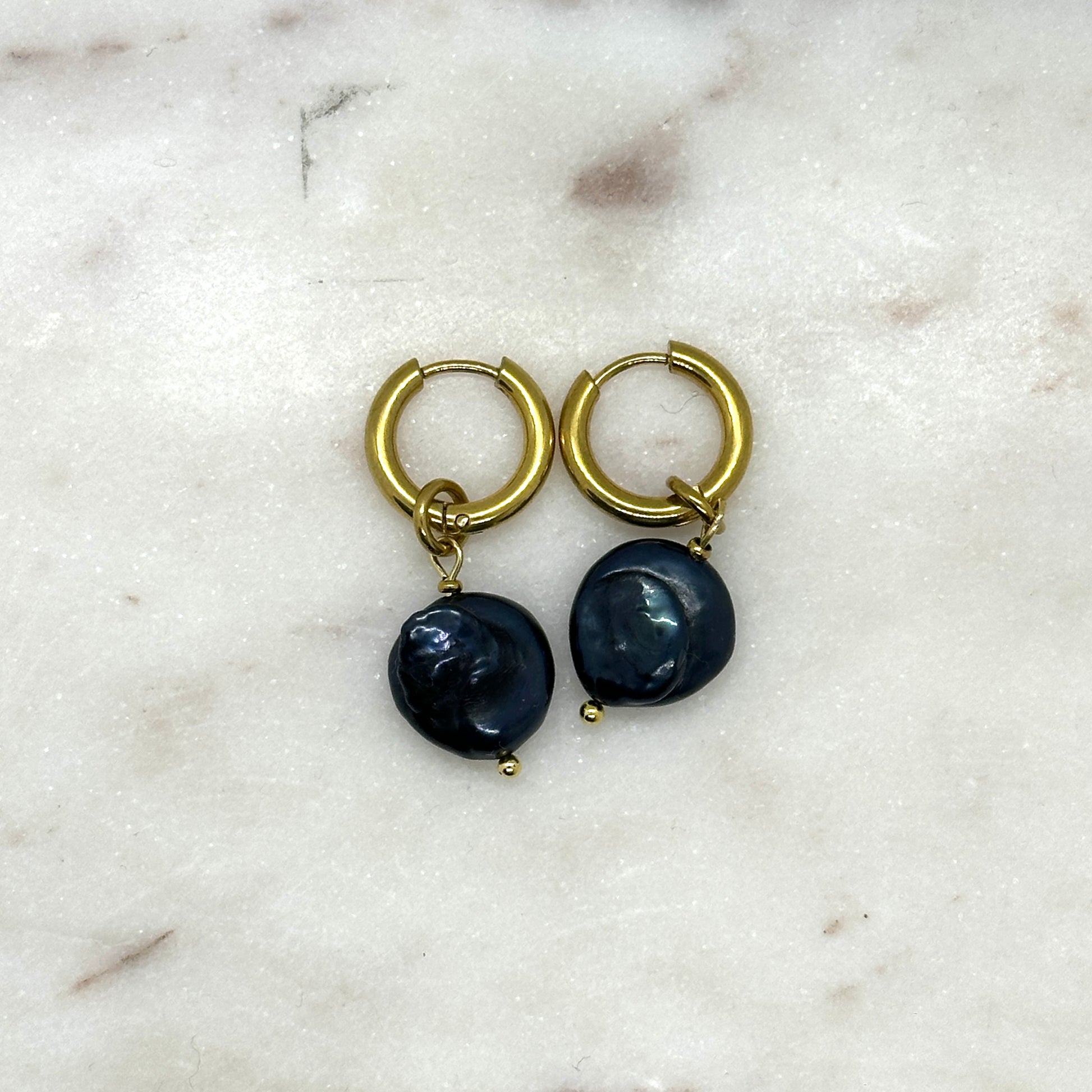 Pair of gold hoop earrings with black pears on a marble surface