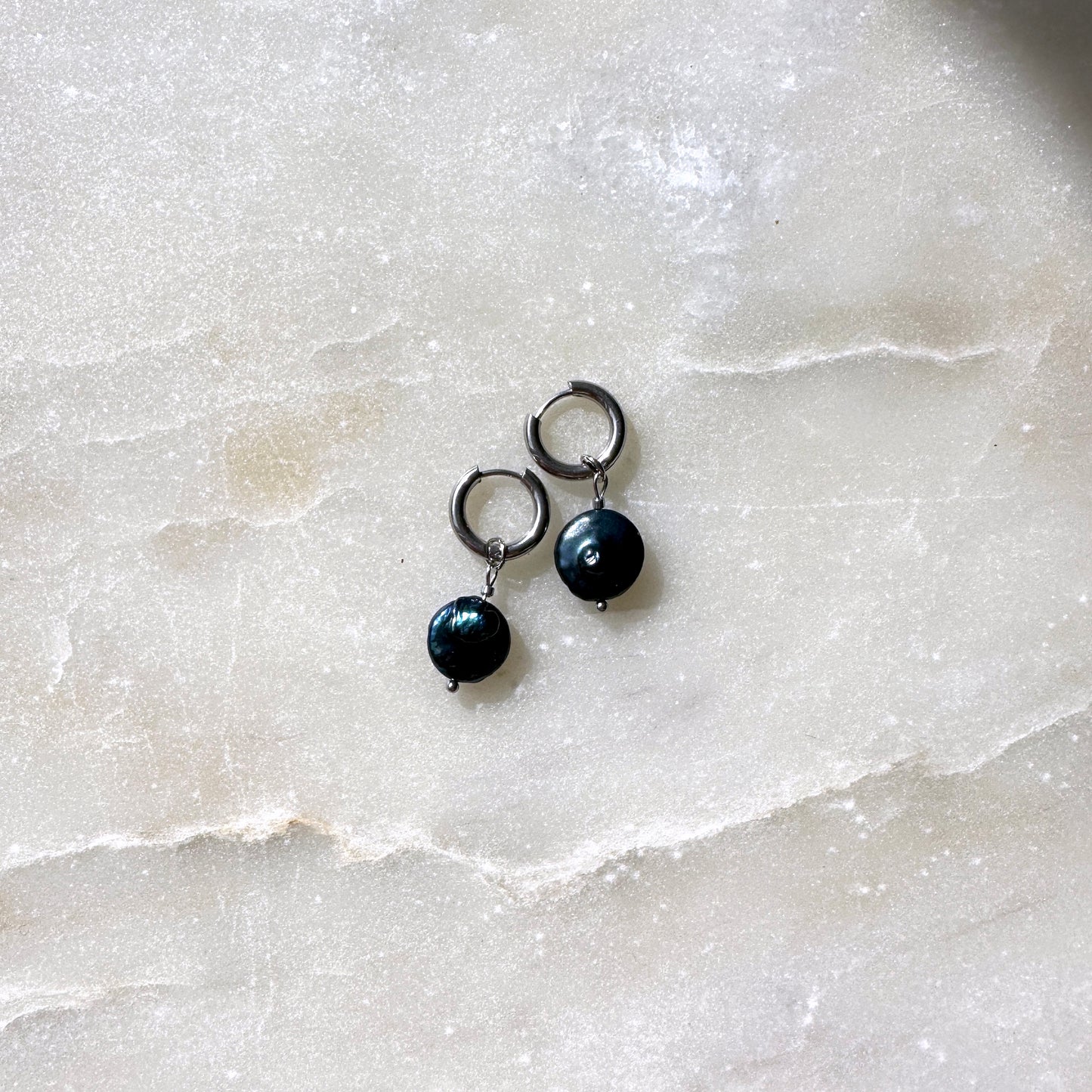 Pair of black pearl earrings on a light marble surface