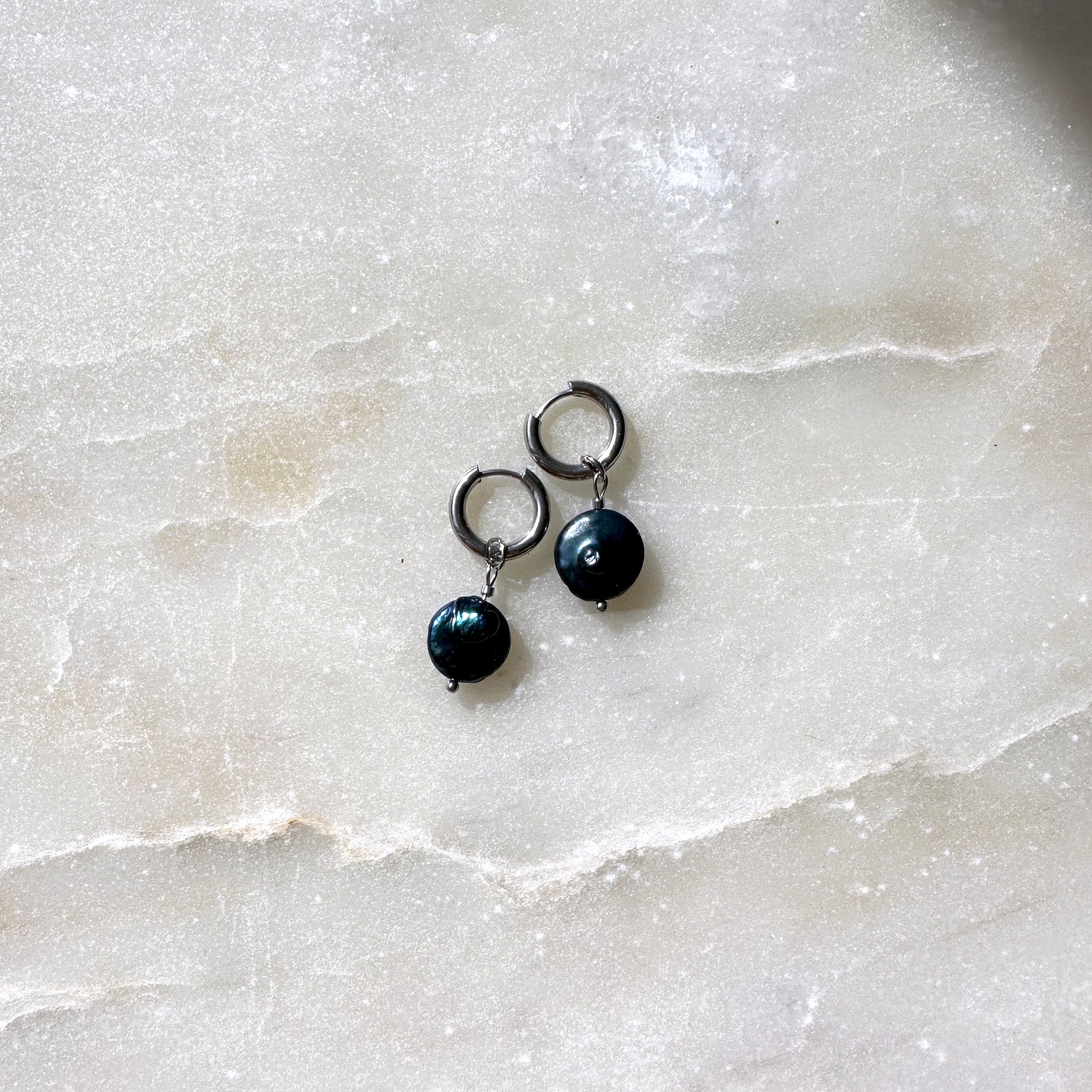 Pair of black pearl earrings on a light marble surface