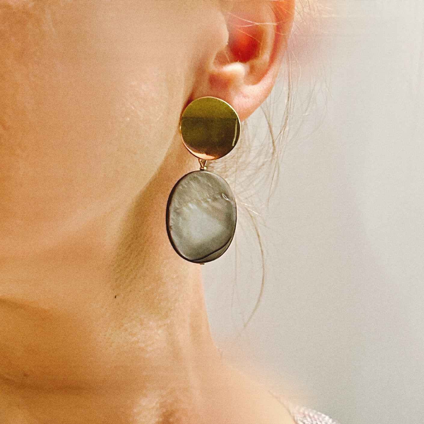 Close-up of an earring with a gold and green stone on a blurred background