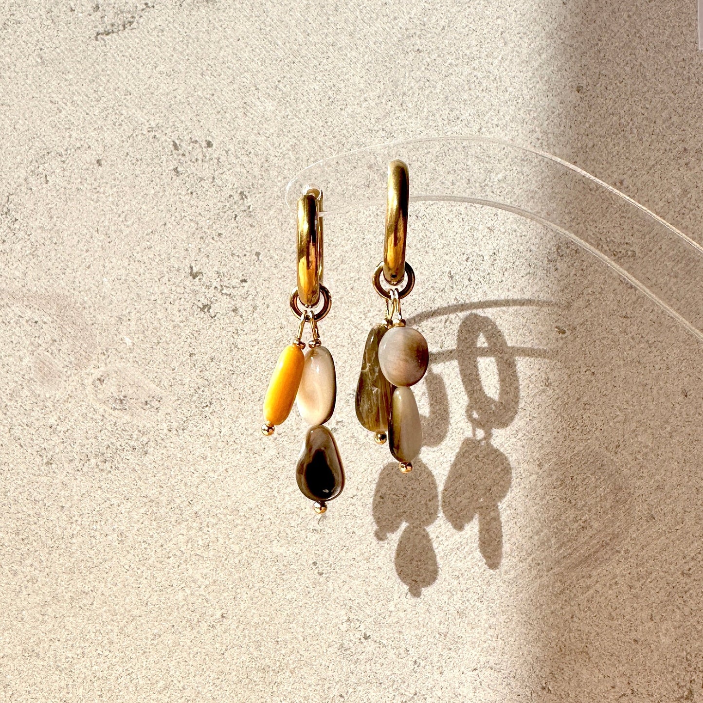 Pair of gold earrings with shell pendants on a textured beige surface