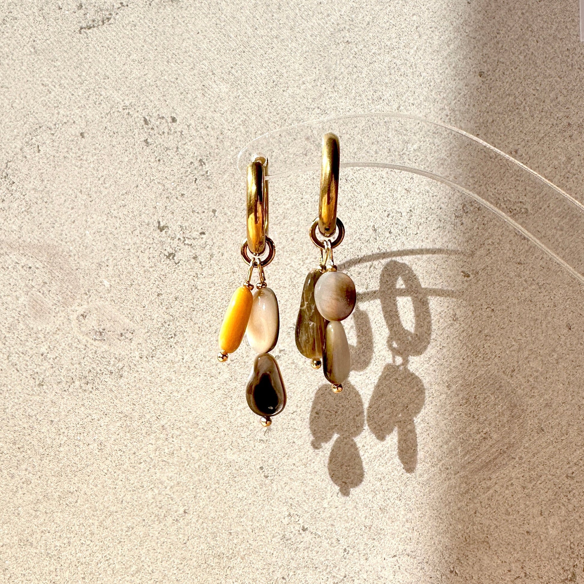 Pair of gold earrings with shell pendants on a textured beige surface