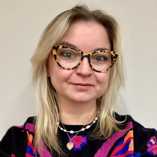 A woman wearing colourful glasses and a sweater against a plain background in two handmade necklaces with stone and pearls