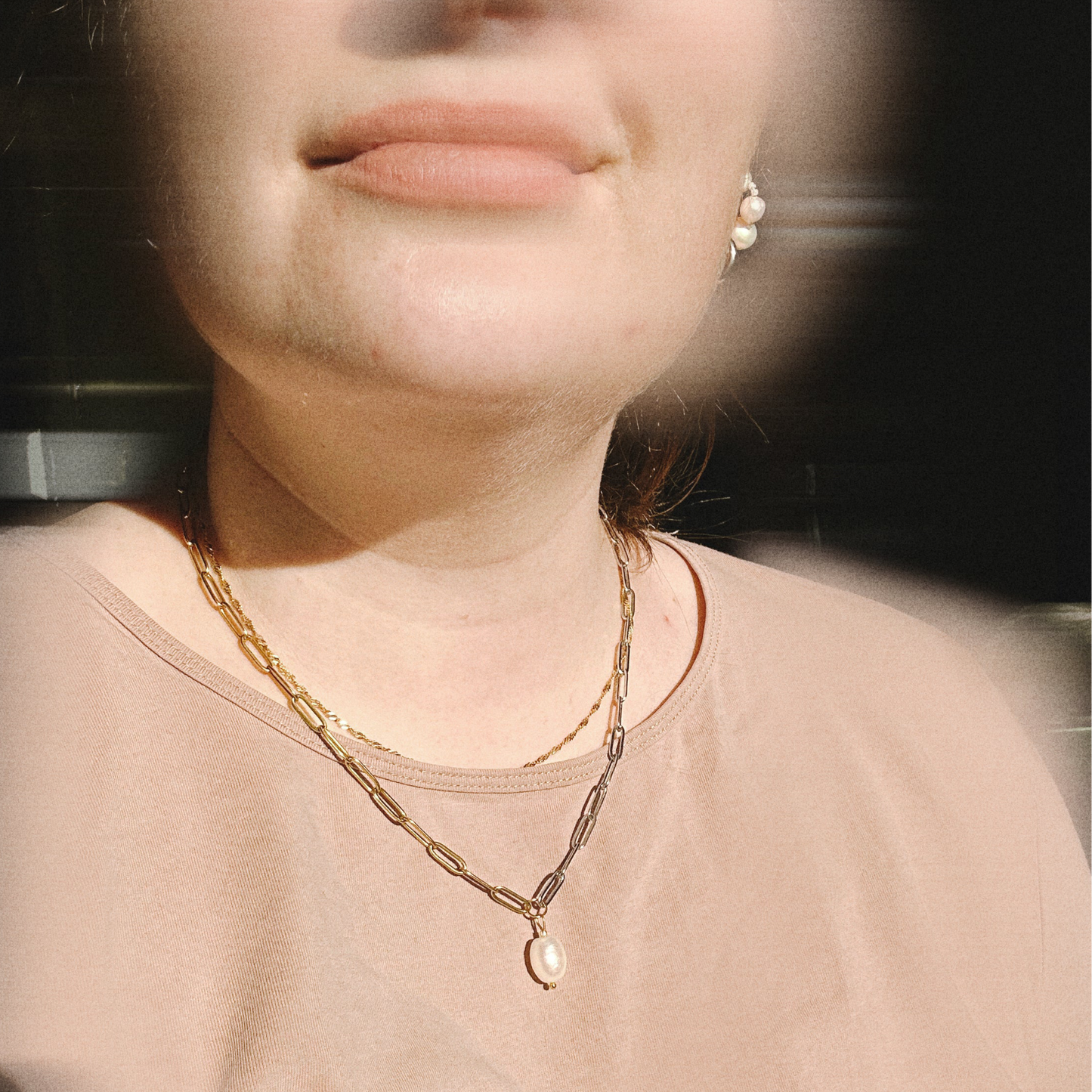 Close-up of a person wearing a half-silver half-gold necklace with a pendant.
