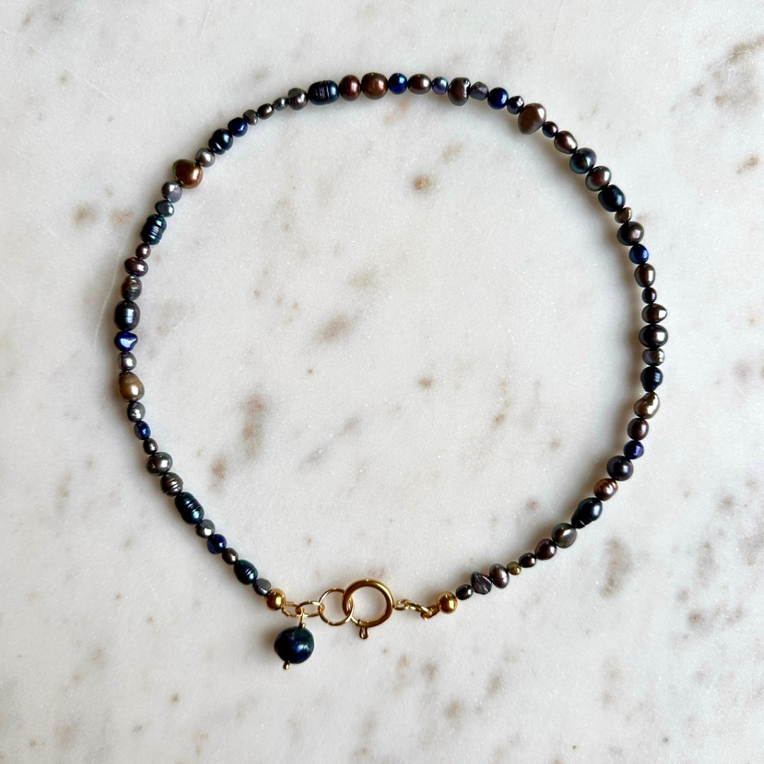 Necklace with dark beads and a gold clasp on a marble surface