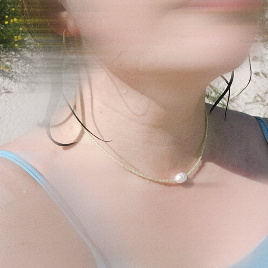 Close-up of a person wearing a delicate gold necklace with a pearl pendant outdoors.