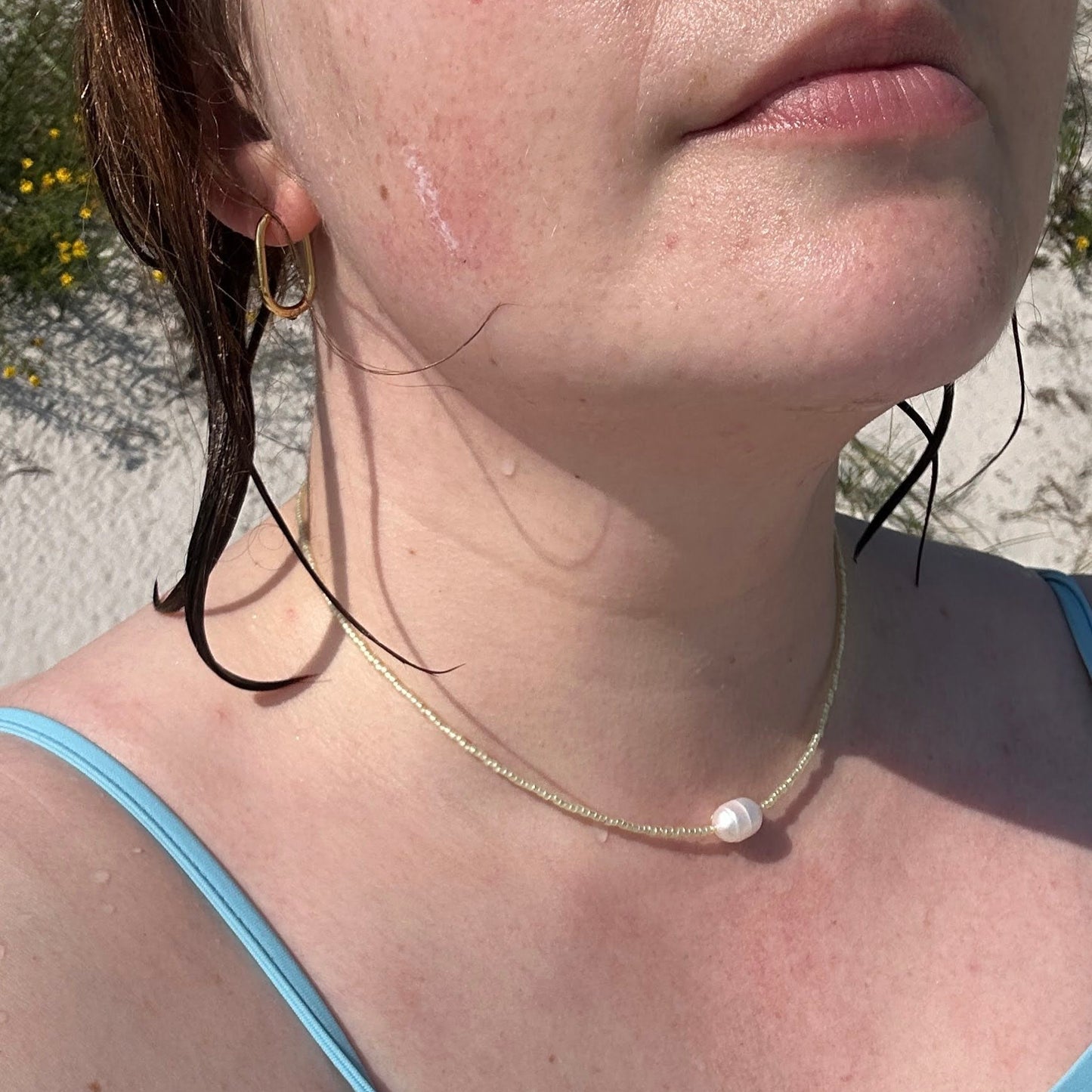 Close-up of a person wearing a light yellow beaded necklace with a pearl in the middle.

