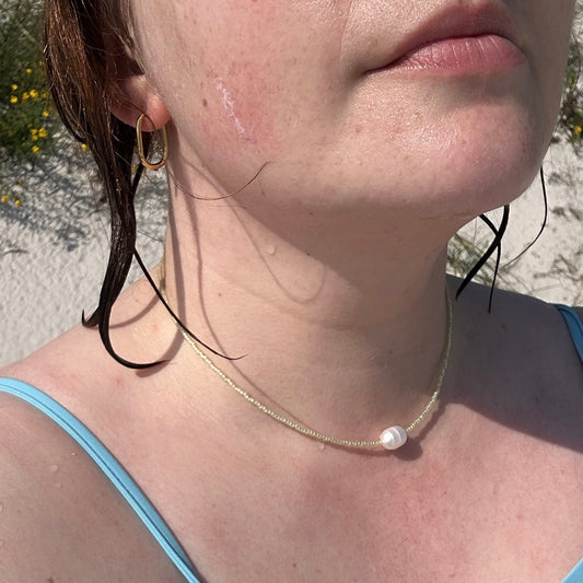 Close-up of a person wearing a light yellow beaded necklace with a pearl in the middle.
