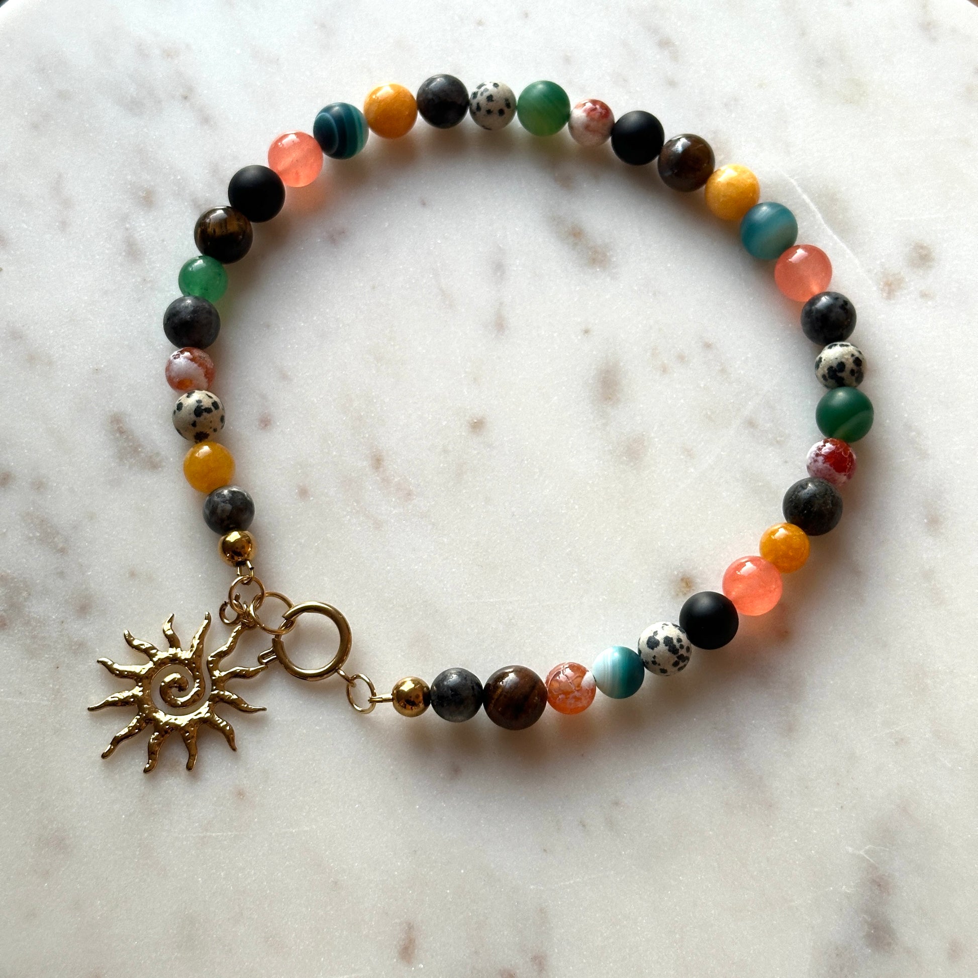 Multicolored beaded bracelet with a sun charm on a marble surface