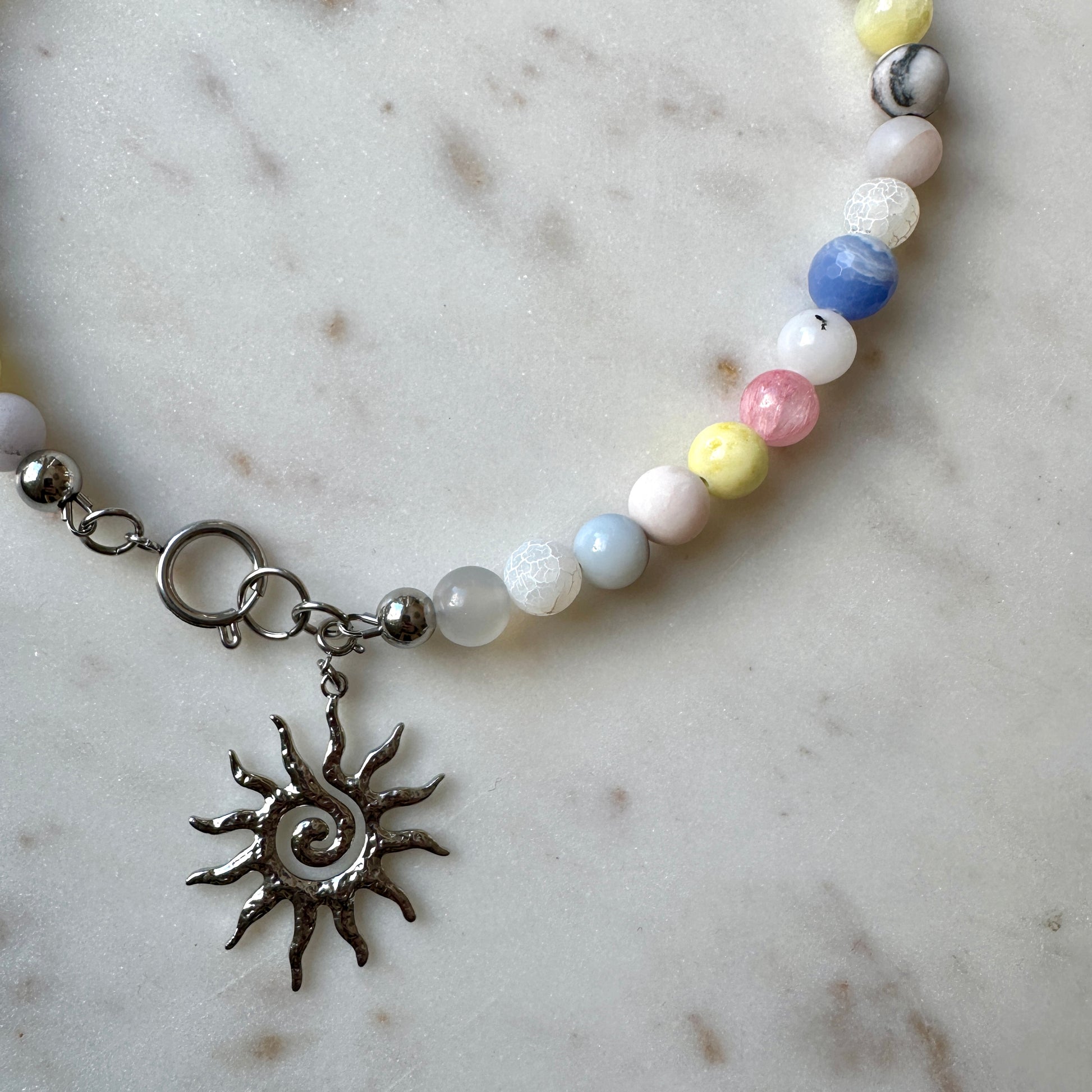 Beaded necklace with a sun charm on a marble surface
