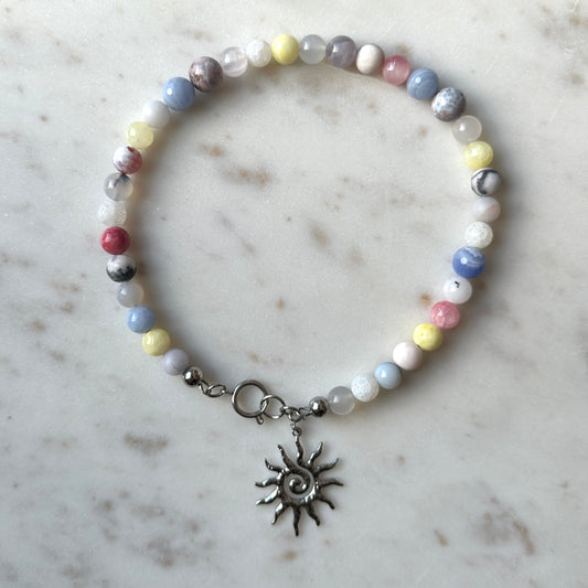 Beaded necklace with colorful stone beads with a sun charm on a marble surface