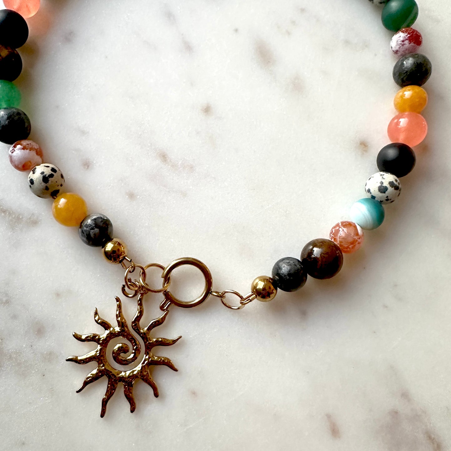 Necklace with multicolored necklace and a sun charm on a marble surface