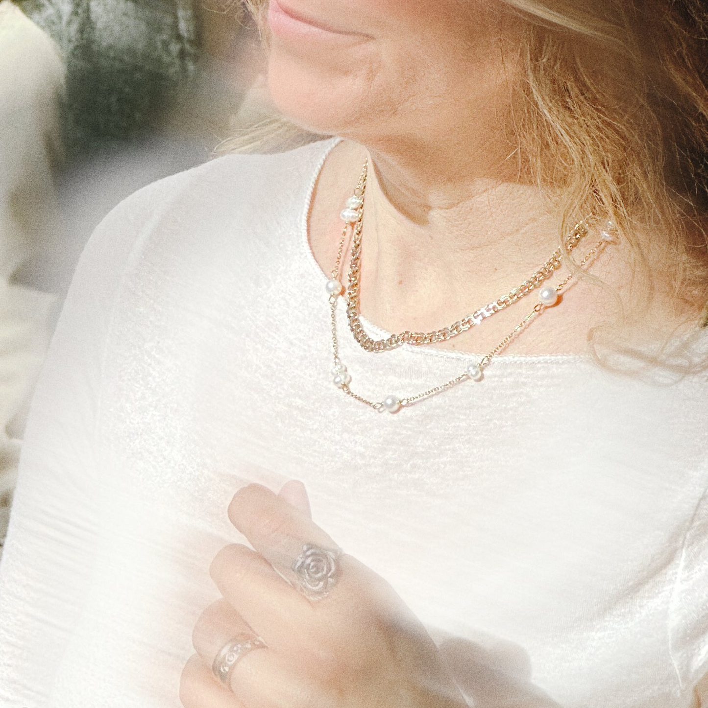 Close-up of a person wearing layered gold necklaces and rings.