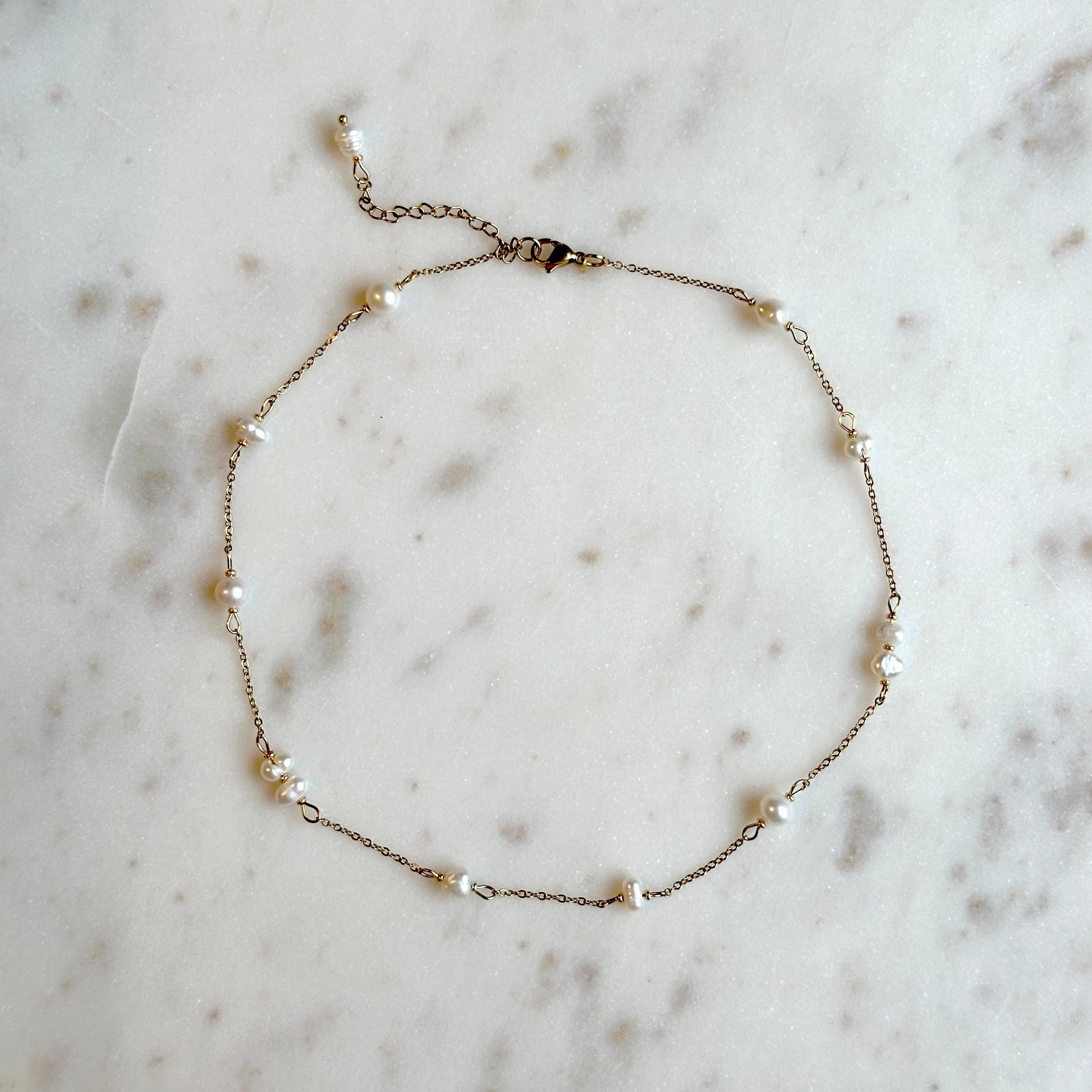 hadmade gold thin necklace with small upcycled pearls lying on a marble surface