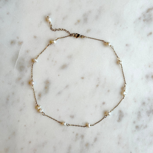 hadmade gold thin necklace with small upcycled pearls lying on a marble surface