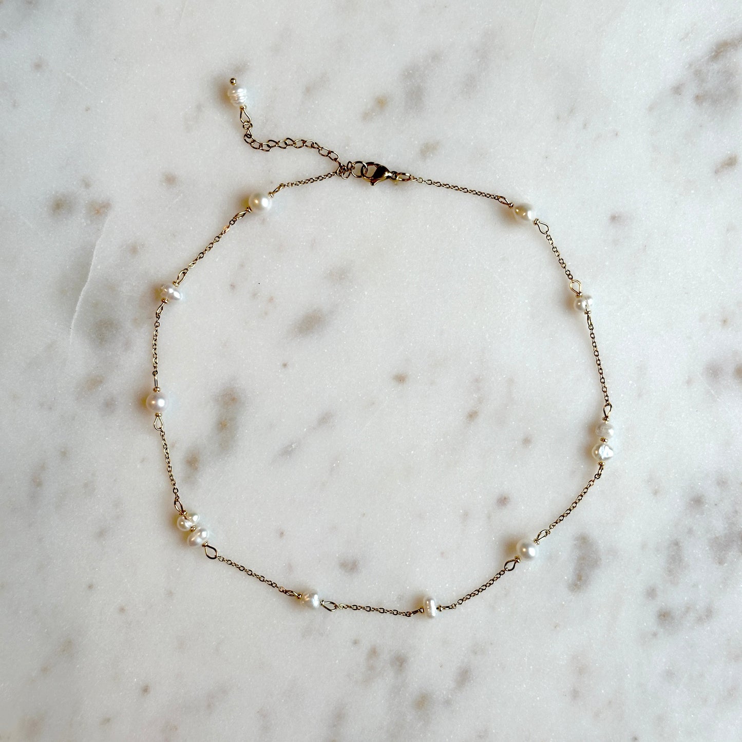 hadmade gold thin necklace with small upcycled pearls lying on a marble surface