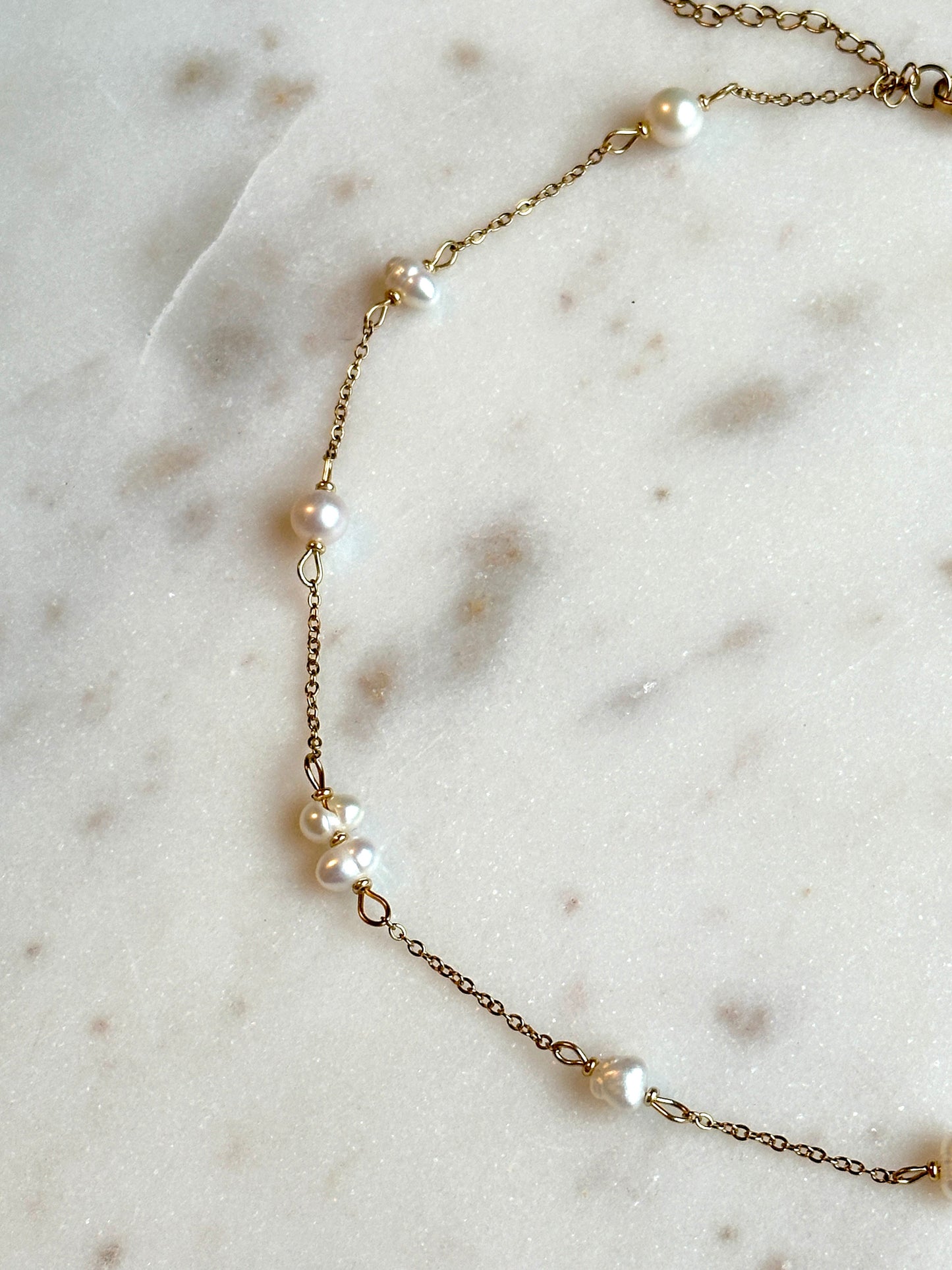 hadmade gold thin necklace with small upcycled pearls lying on a marble surface