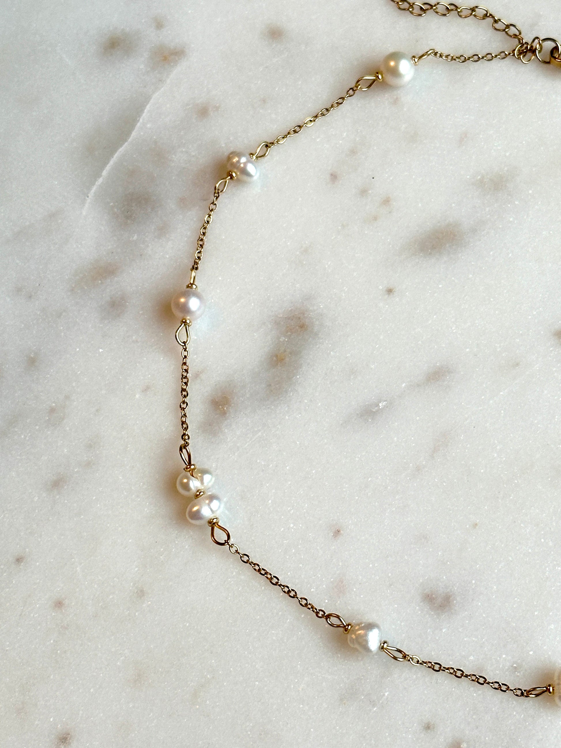 hadmade gold thin necklace with small upcycled pearls lying on a marble surface