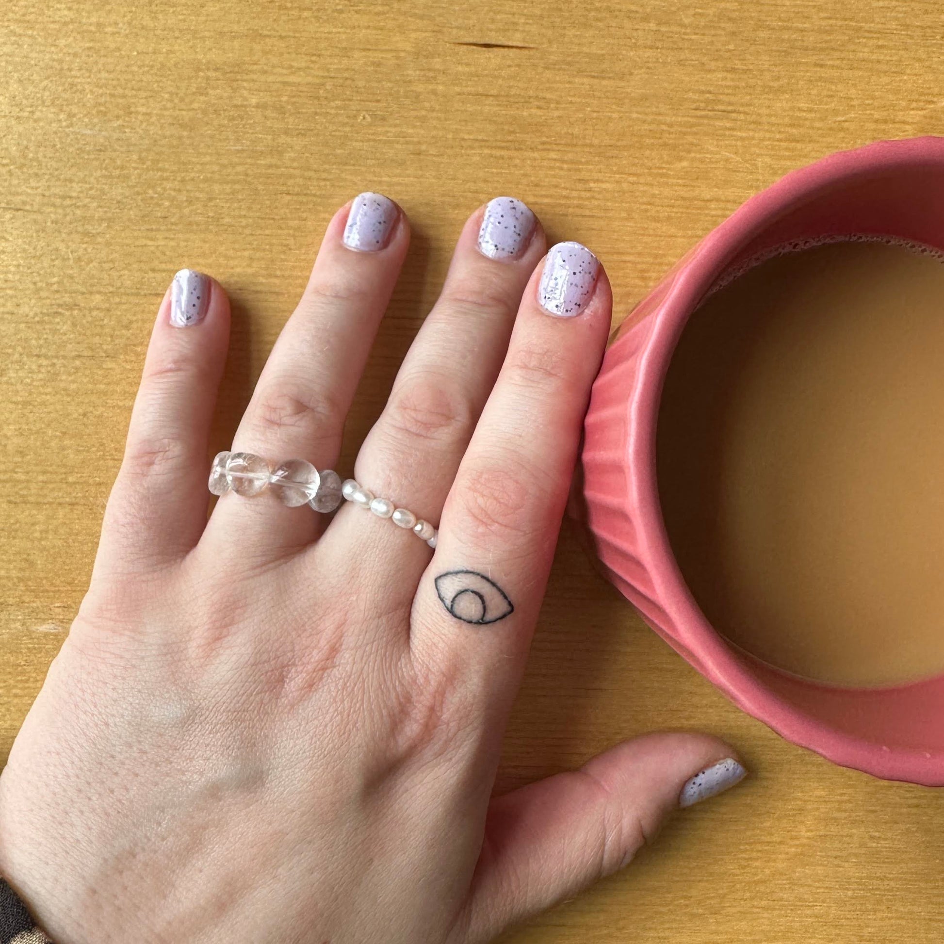 Hand with a ring on a wooden surface next to a pink container