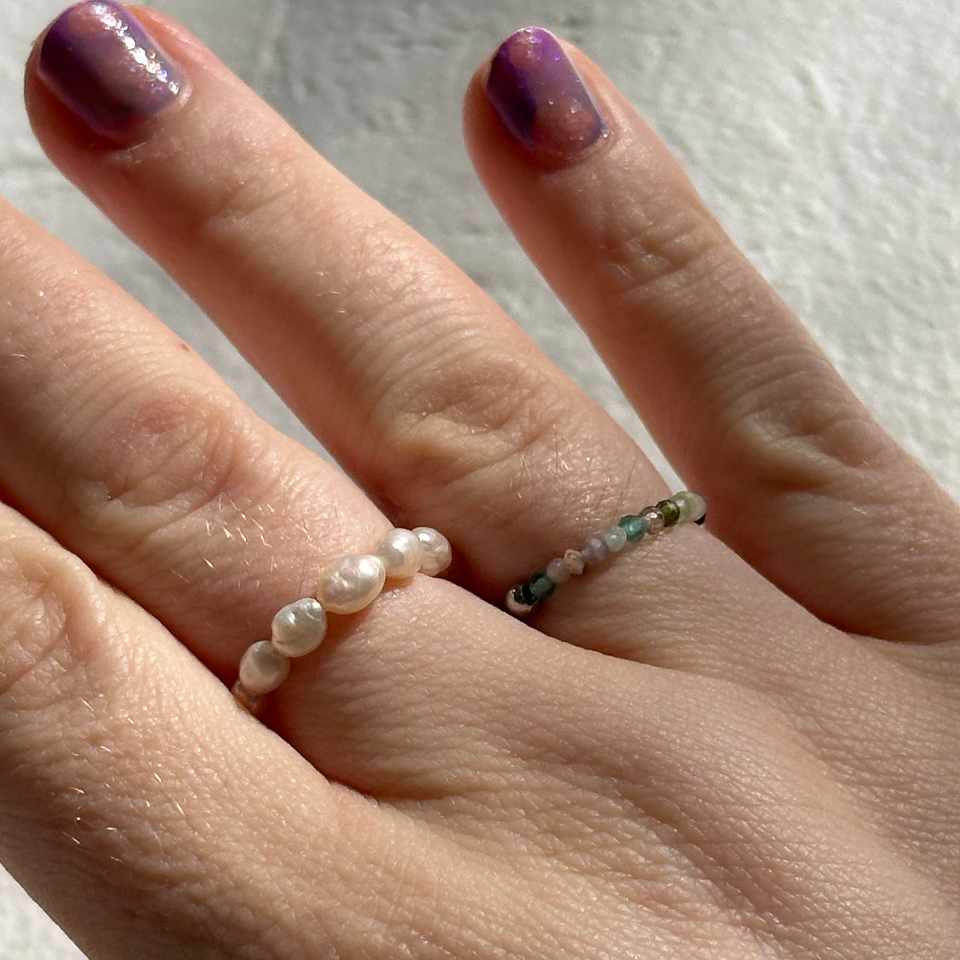 Hand wearing two rings with pearls on a neutral background