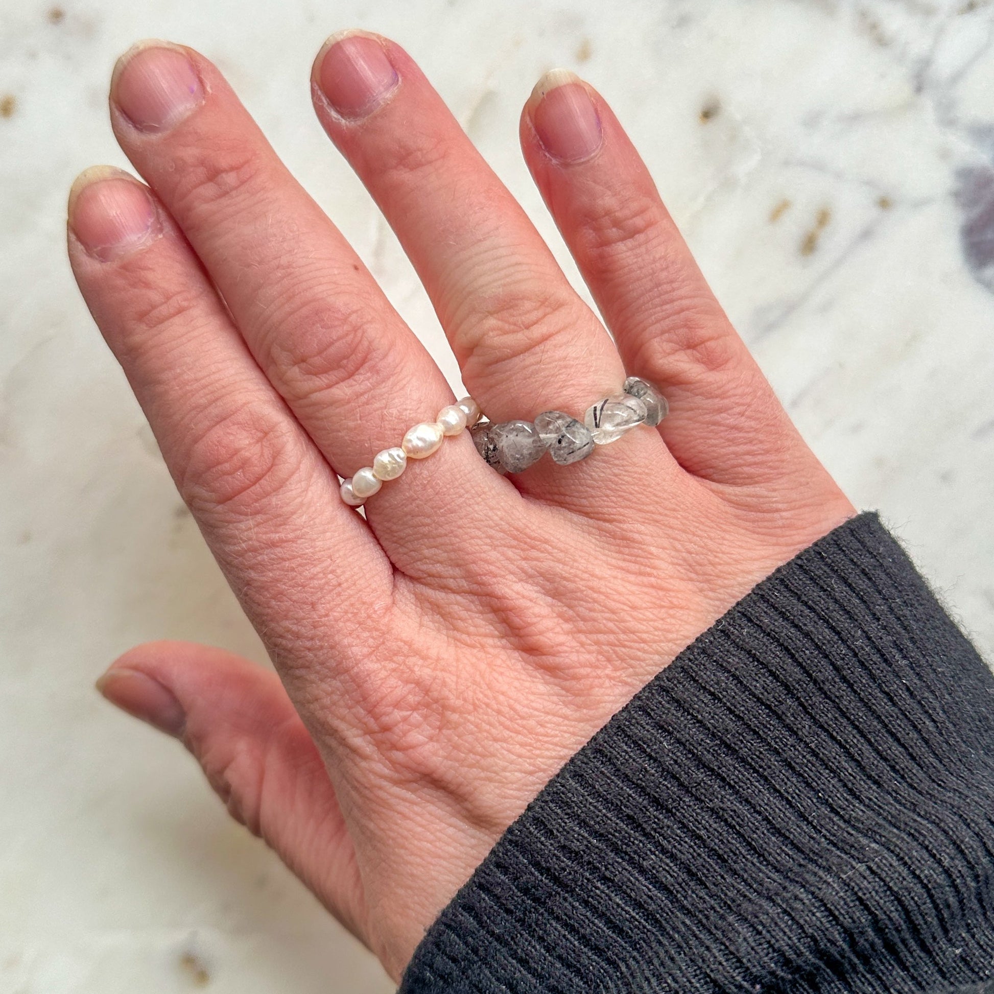 Hand wearing two rings on a marble surface